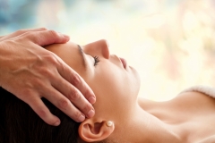 44647487 - close up head portrait of young woman having facial massage in spa. therapist massaging woman’s head against colorful background.